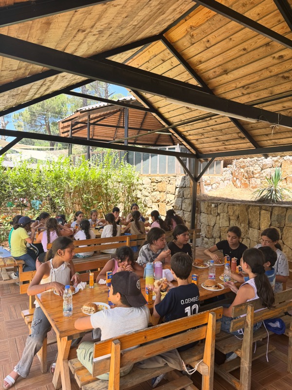 Children eating lunch together under a wooden shelter